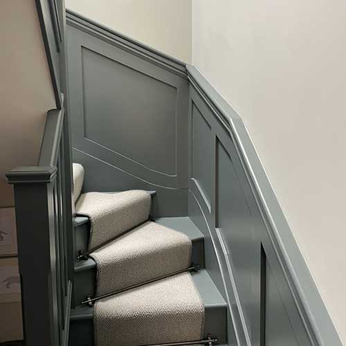 Grey panelled staircase with carpet runner and stair rods