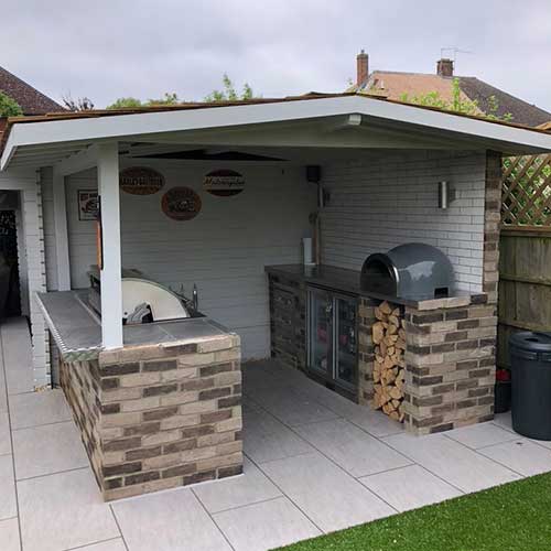 Covered outdoor kitchen with brick bar, pizza oven and porcelain patio