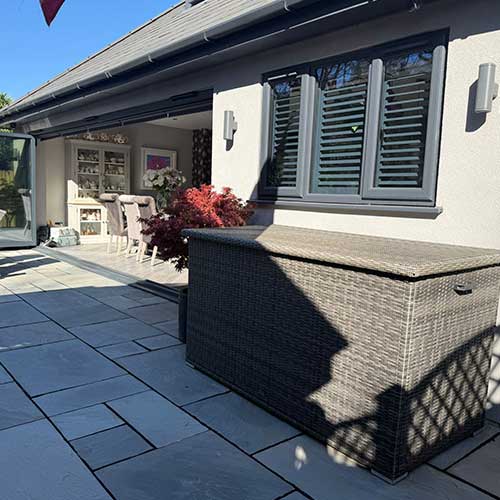 Bi-fold doors and shuttered windows onto grey paved patio