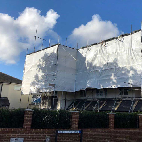 Two-storey house wrapped in scaffolding and white sheeting during roof works
