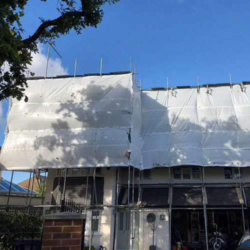 Detached house under scaffolding with protective shrink-wrap covering the roof