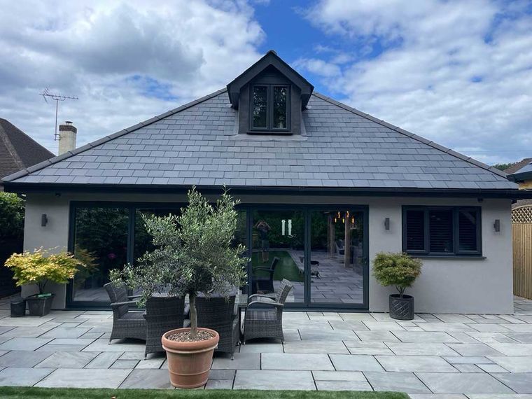 Rendered rear extension with sliding doors beneath a slate roof with a dormer