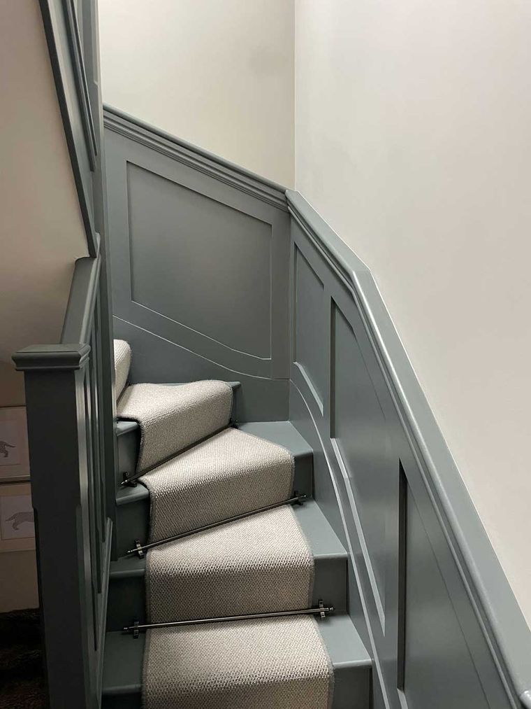 Grey panelled staircase with a carpet runner and stair rods