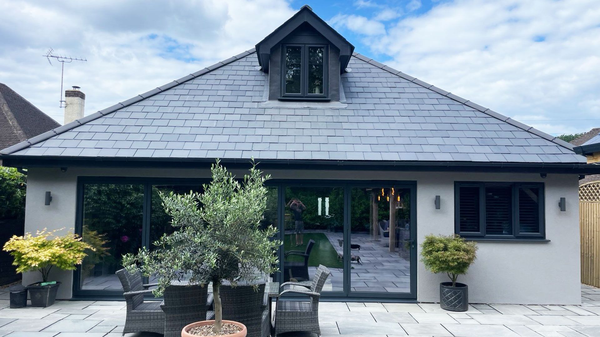 Rendered rear extension with sliding doors beneath a slate roof with a dormer